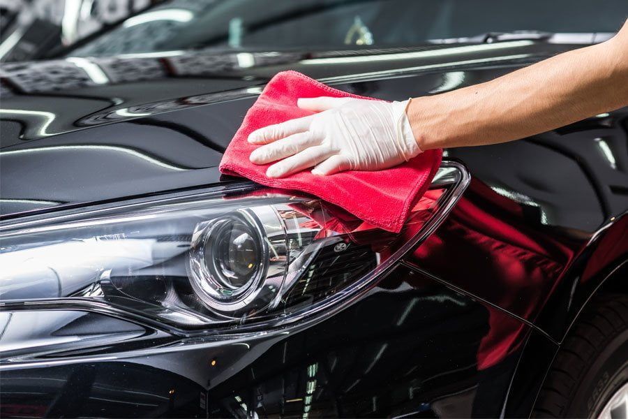 A man using a microfiber cloth to wipe away dirt on a shiny car.