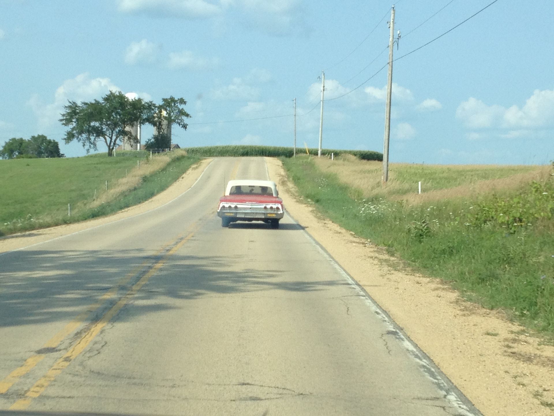 Restored classic car driving along scenic rural road, showcasing vintage auto restoration
