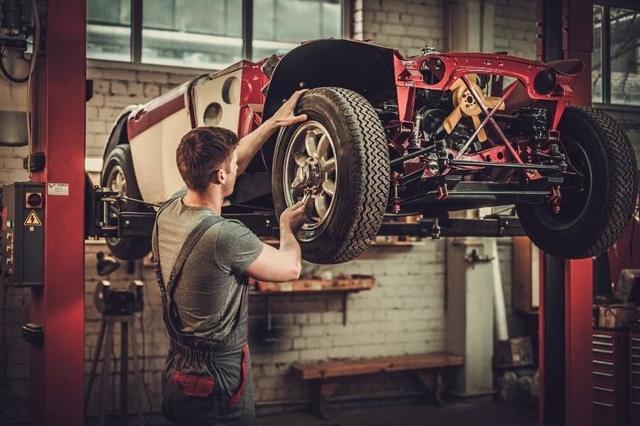Auto restoration technician working on classic car suspension and wheel assembly