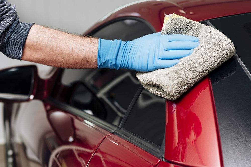Gloved hand wiping a red car with a microfiber cloth during cleaning