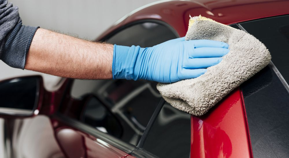 Gloved hand wiping a red car with a microfiber cloth