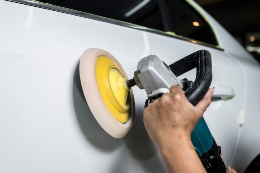Technician polishing a car’s painted surface with a power buffer to restore shine and smooth finish.