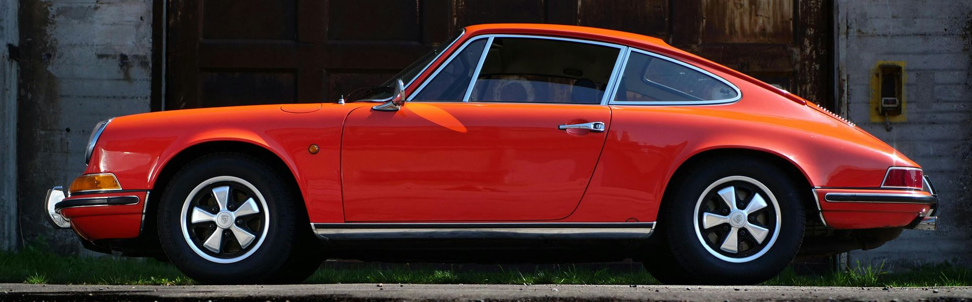 Red vintage coupe parked side view against a brick wall.