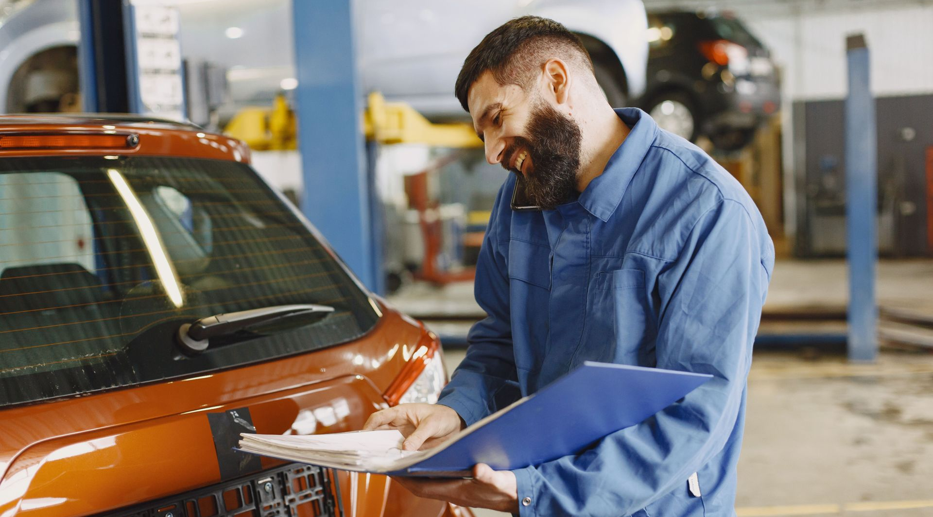 Mechanic inspecting the front of an orange car in a garage workshop