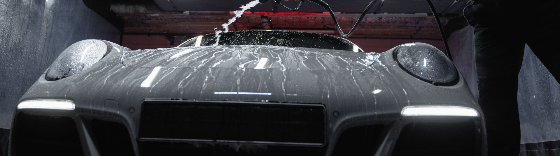 Black sports car front view with water spraying across the windshield in a dark setting