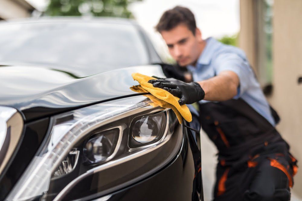 Detailing technician wiping a black car’s front end to enhance shine and finish during auto detailing.