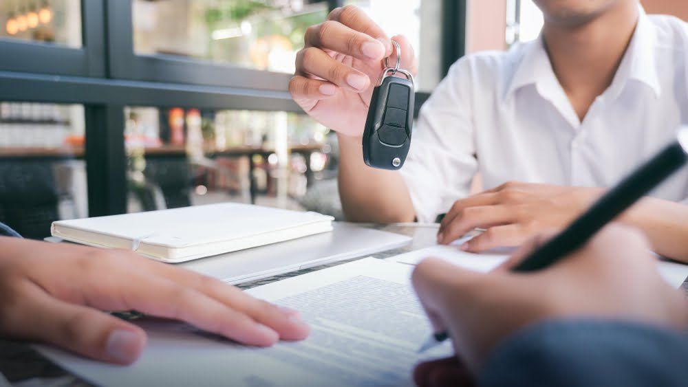 a gentleman in a white shirt passes a spare key to the new owner helping him to learn how to increase the value of your car