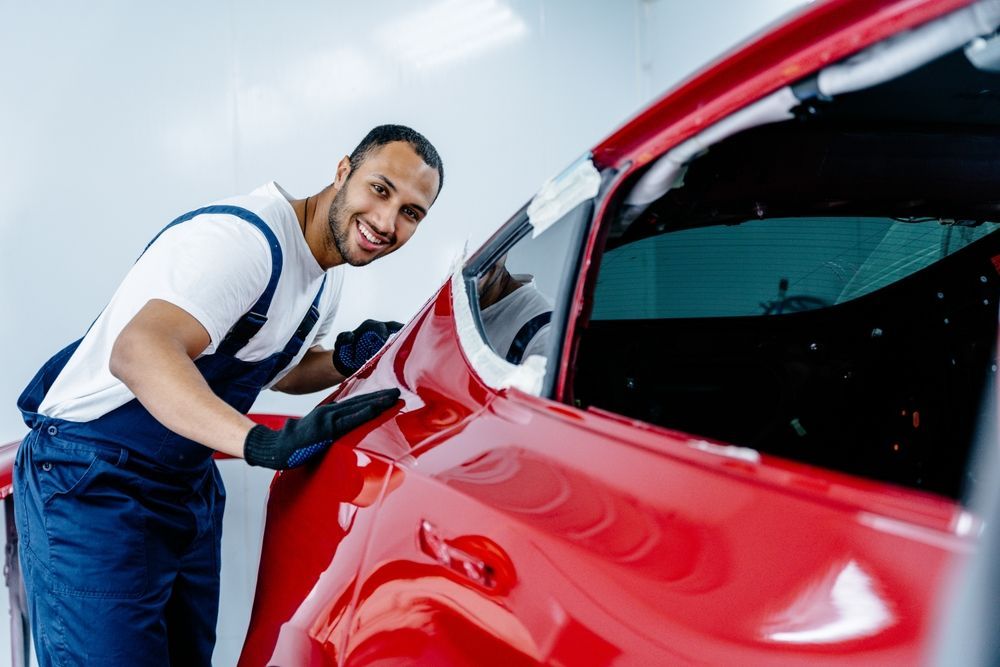 Smiling auto body technician polishing red car after collision repair in paint booth