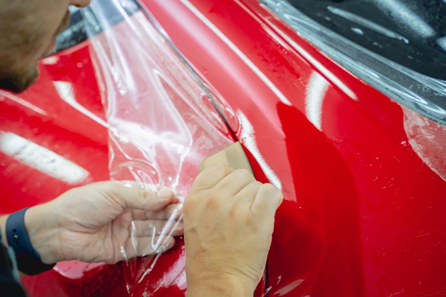 A man is wrapping a red car with clear plastic.