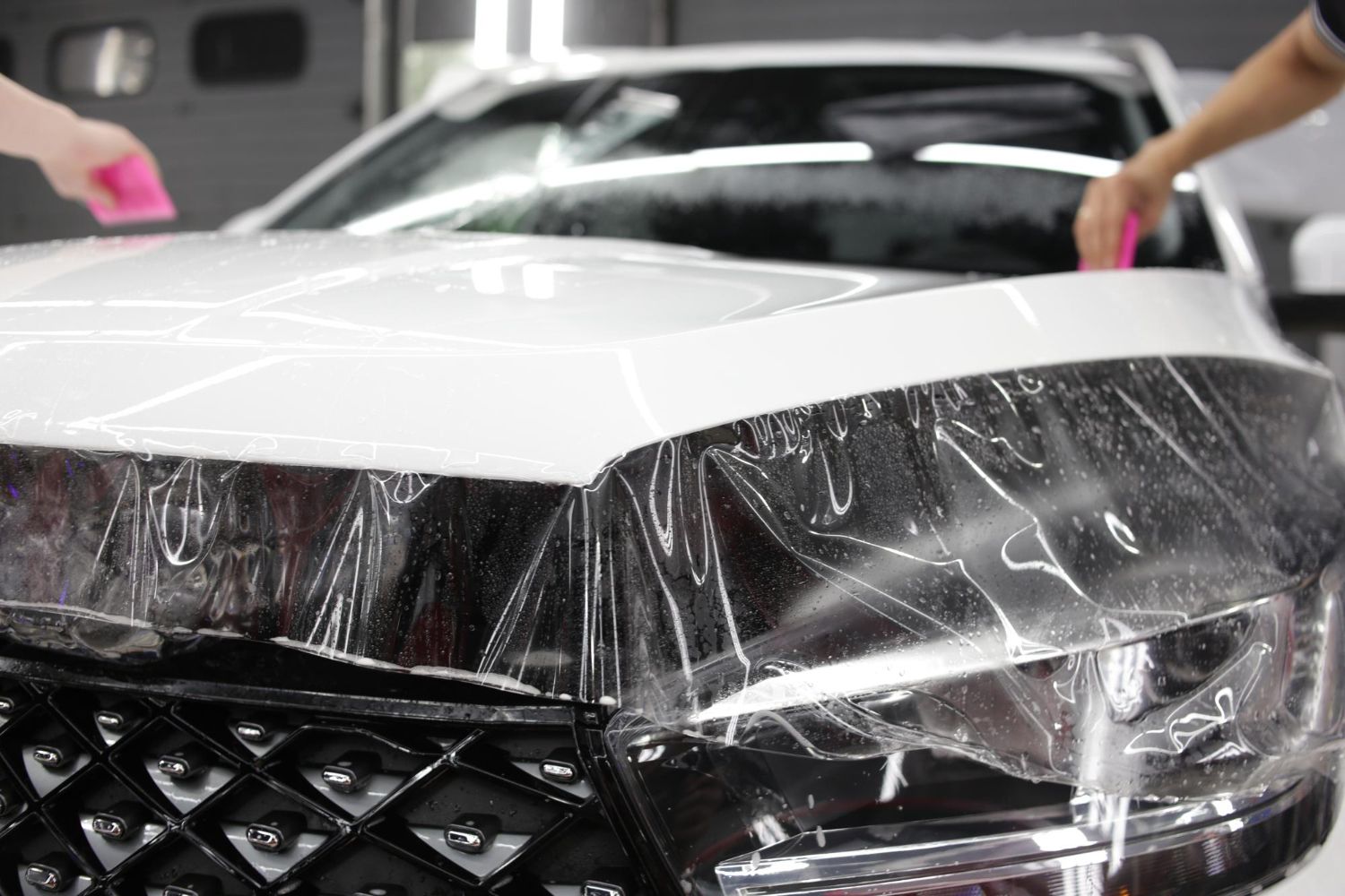 A person is covering the hood of a car with plastic wrap.