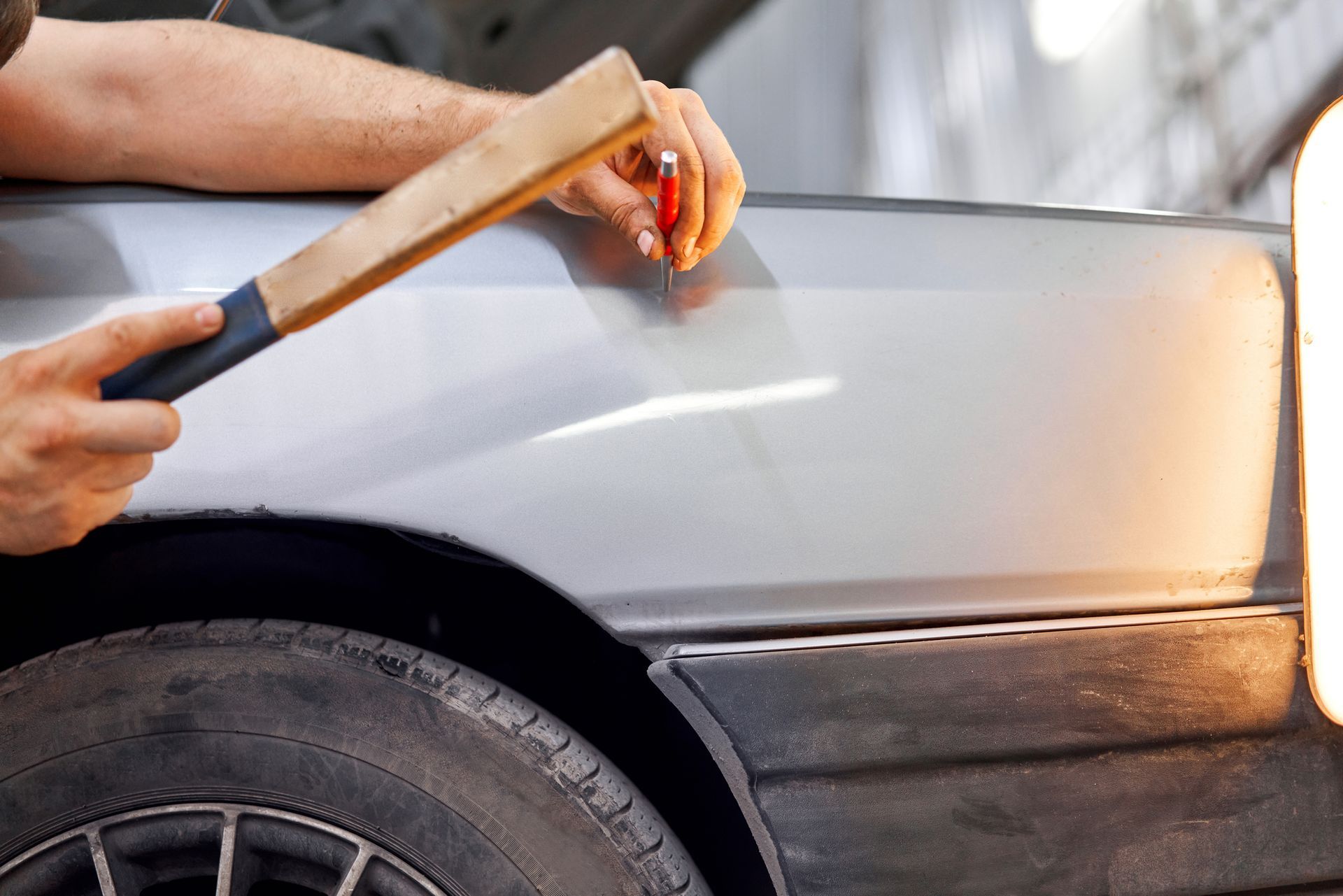 A man is hitting a car with a wooden hammer.