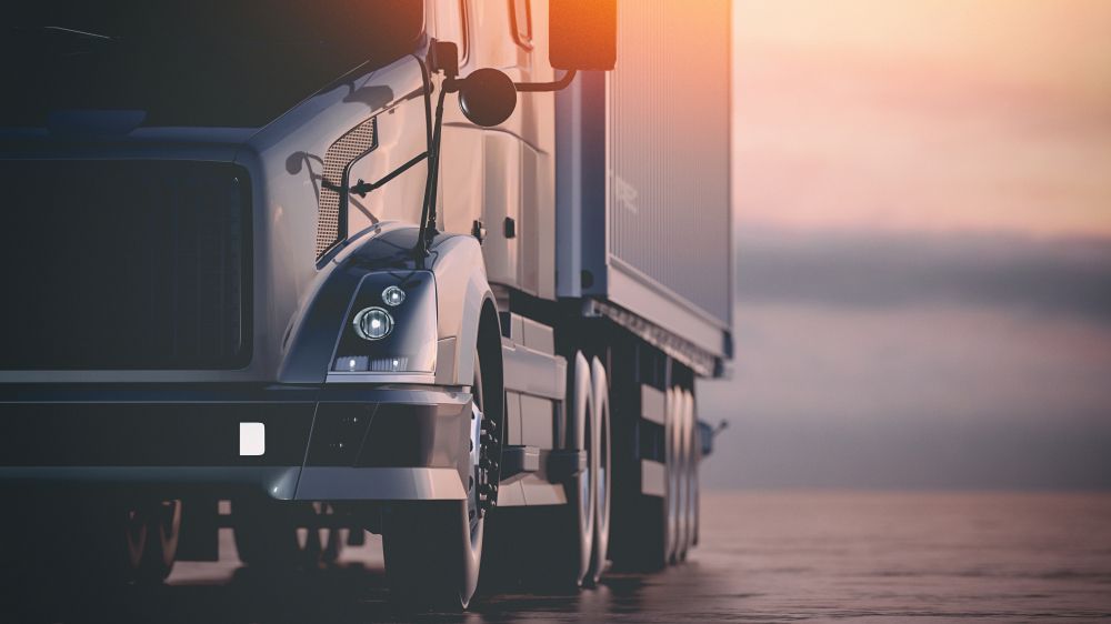 A semi truck is driving down a road next to a body of water at sunset — Reliable Driver Training in Darwin, NT