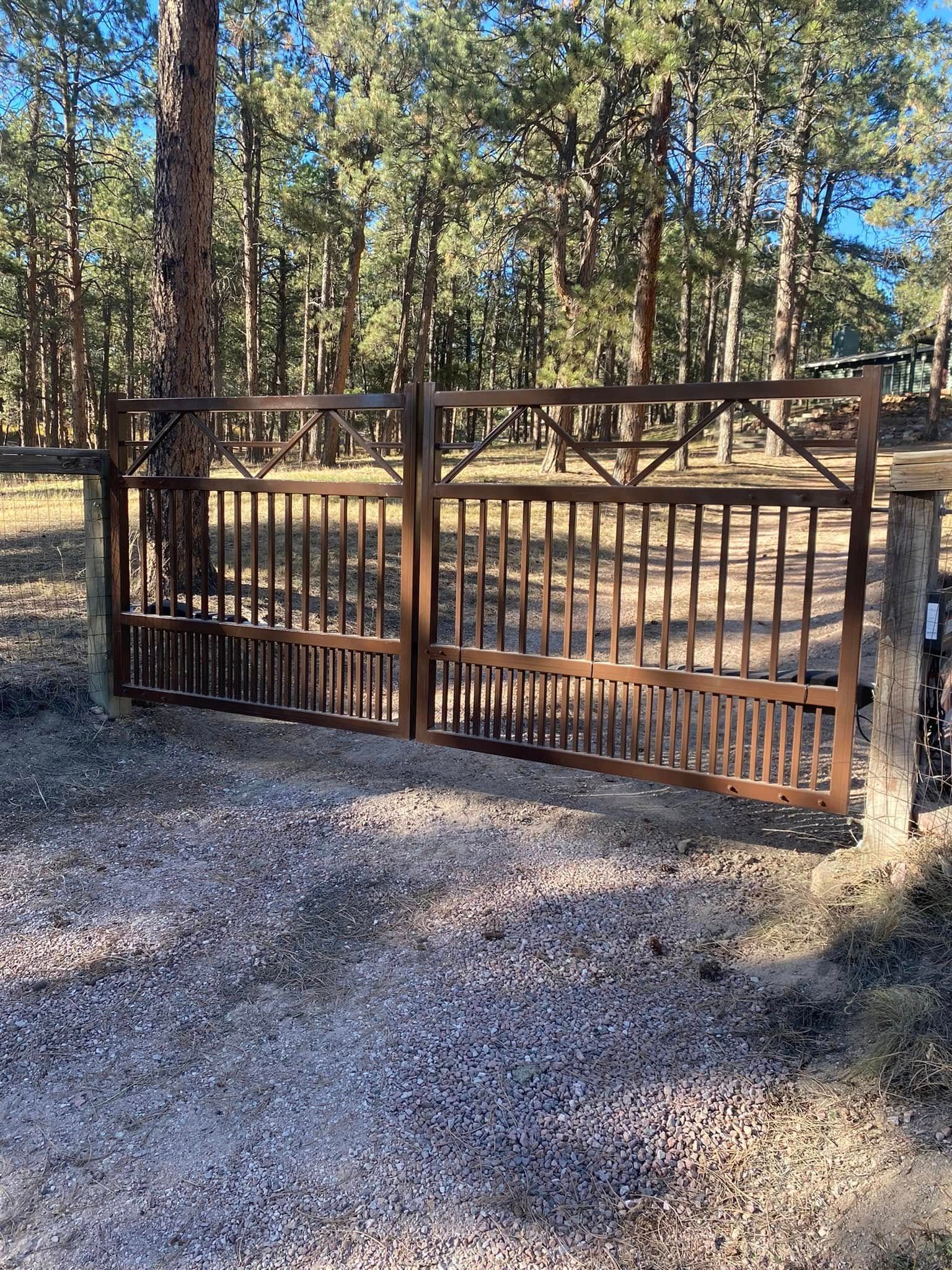 Rustic metal gate at a gravel driveway entrance in a wooded area