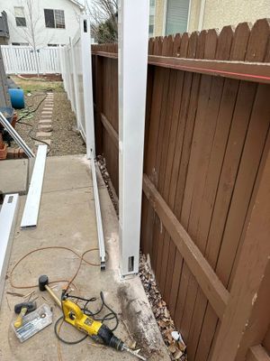 Narrow concrete walkway beside white and brown fences, with tools and debris on the ground.