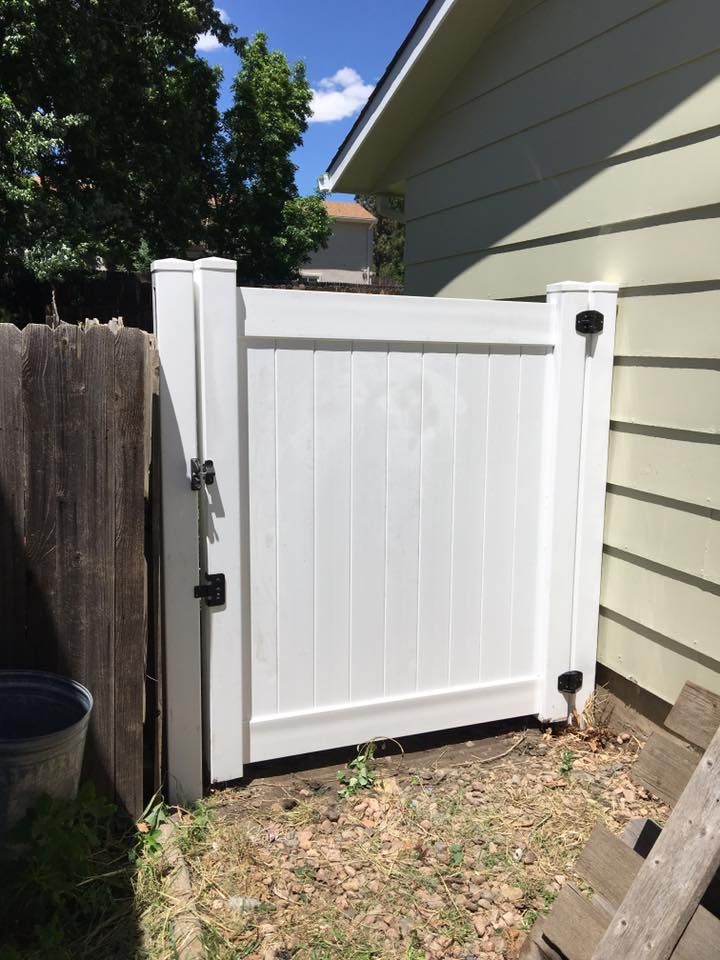 White vinyl gate beside a wooden fence and house siding in a sunny backyard