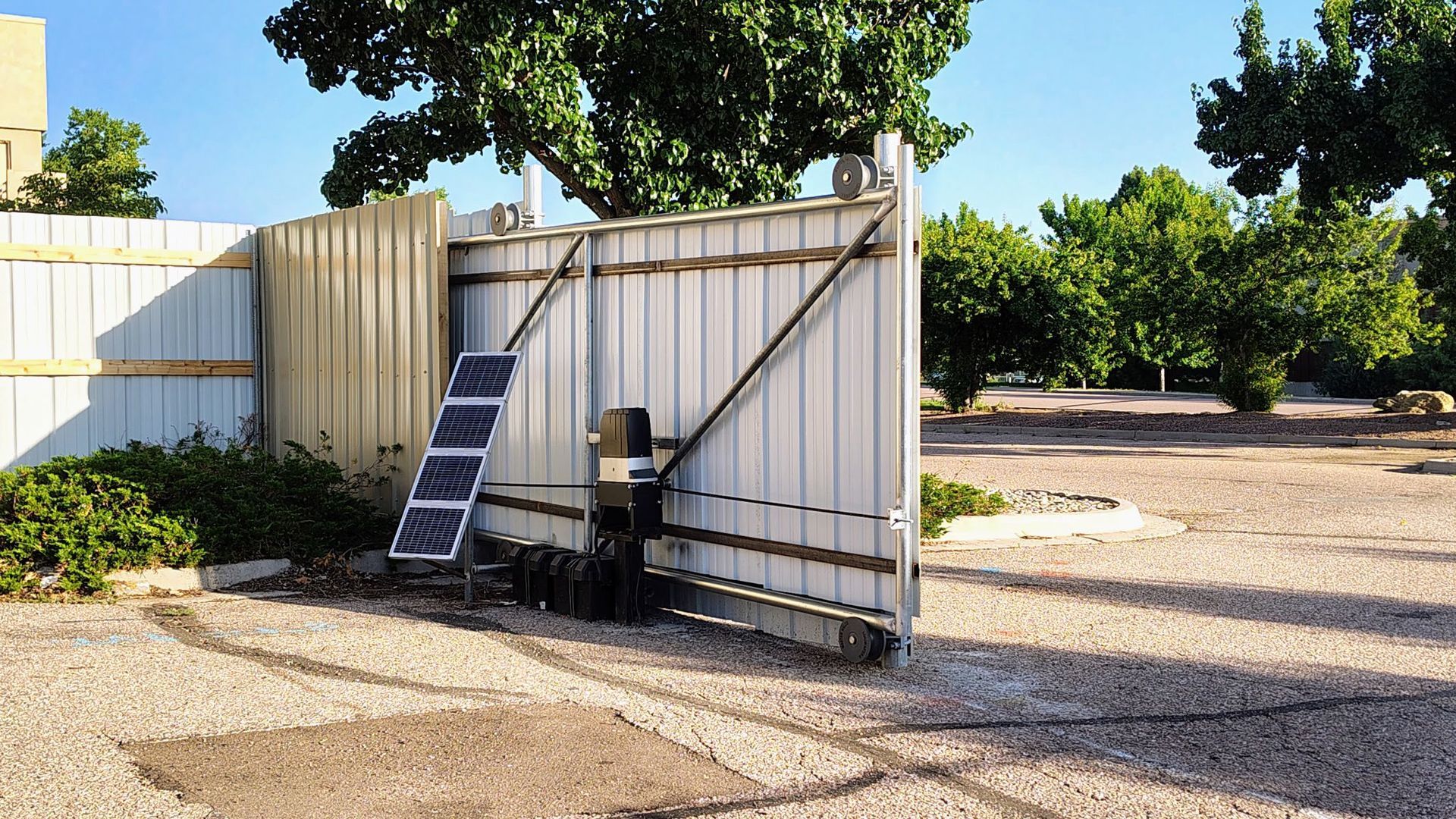 Open shed with a ladder, chair, and grill beside a gravel driveway and trees
