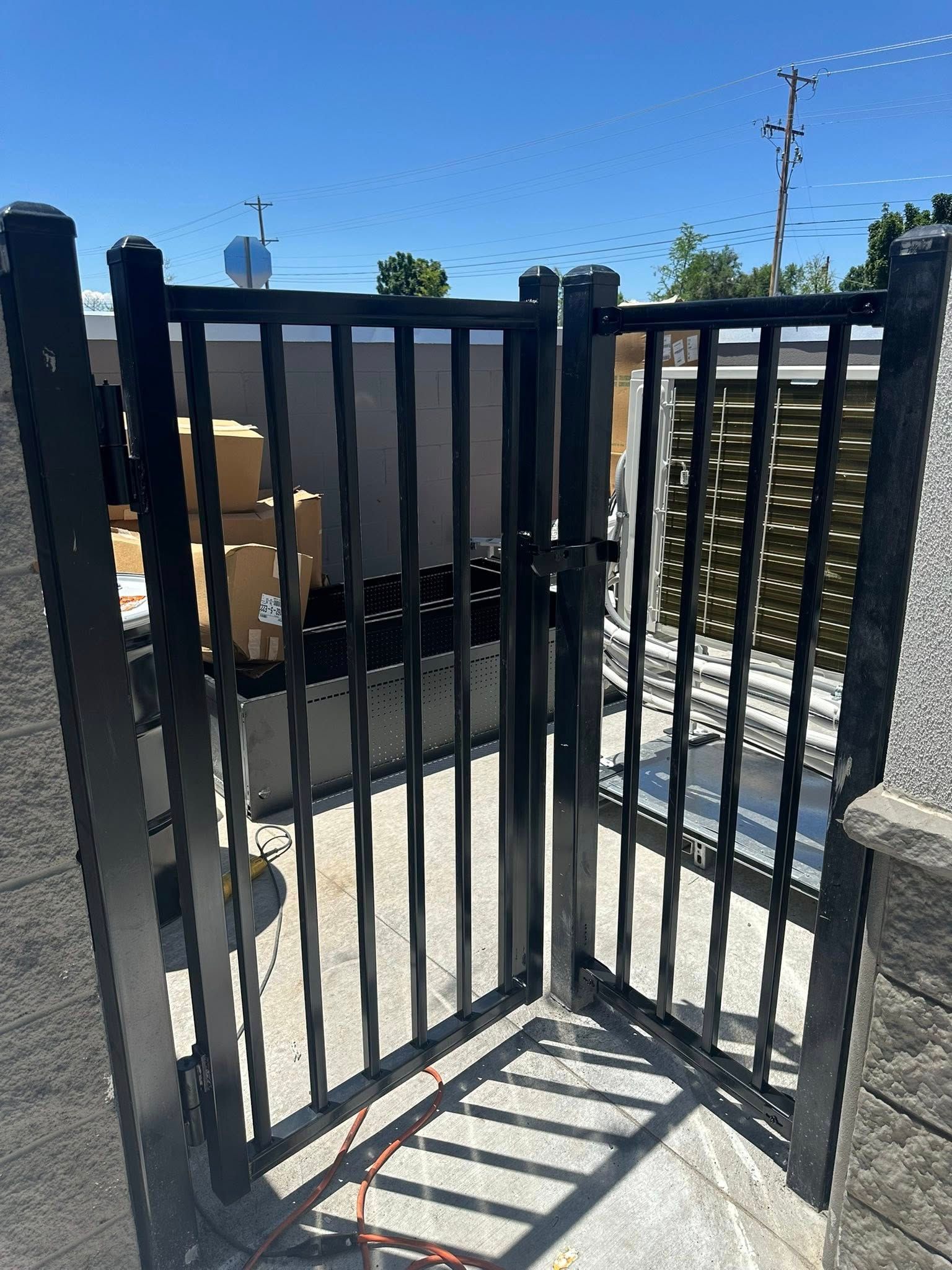 Black metal gate in a sunny outdoor yard with a shadow on the ground and blue sky above