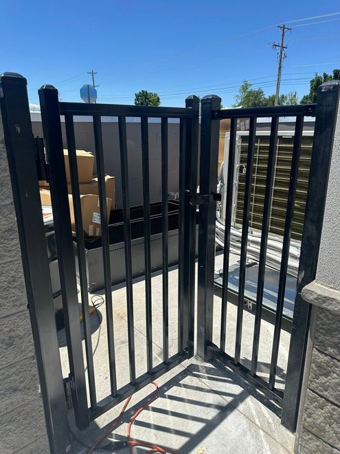 Black metal security gate beside a driveway under a sunny blue sky