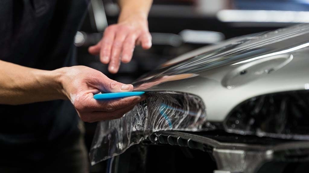 Person applying clear protective film to a car hood.