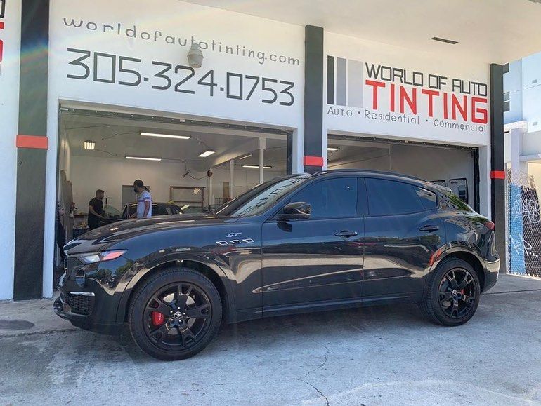 Black SUV parked in front of a tint shop with tinted windows and black wheels; shop sign visible.