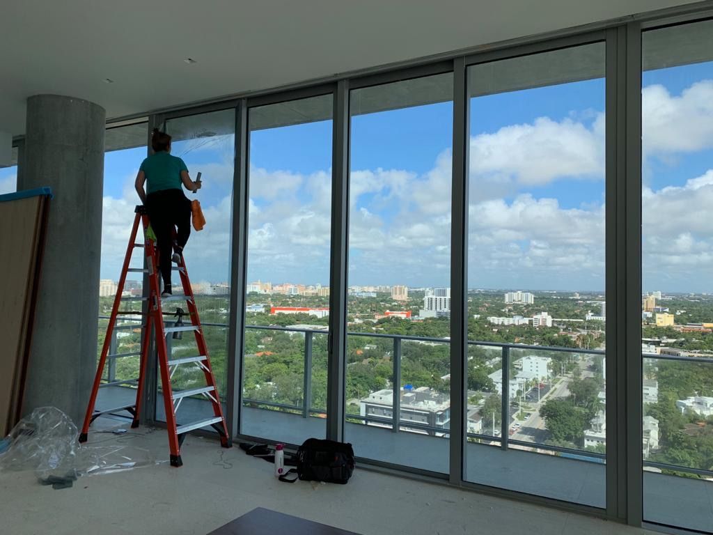 Person on ladder cleaning large windows with city view.