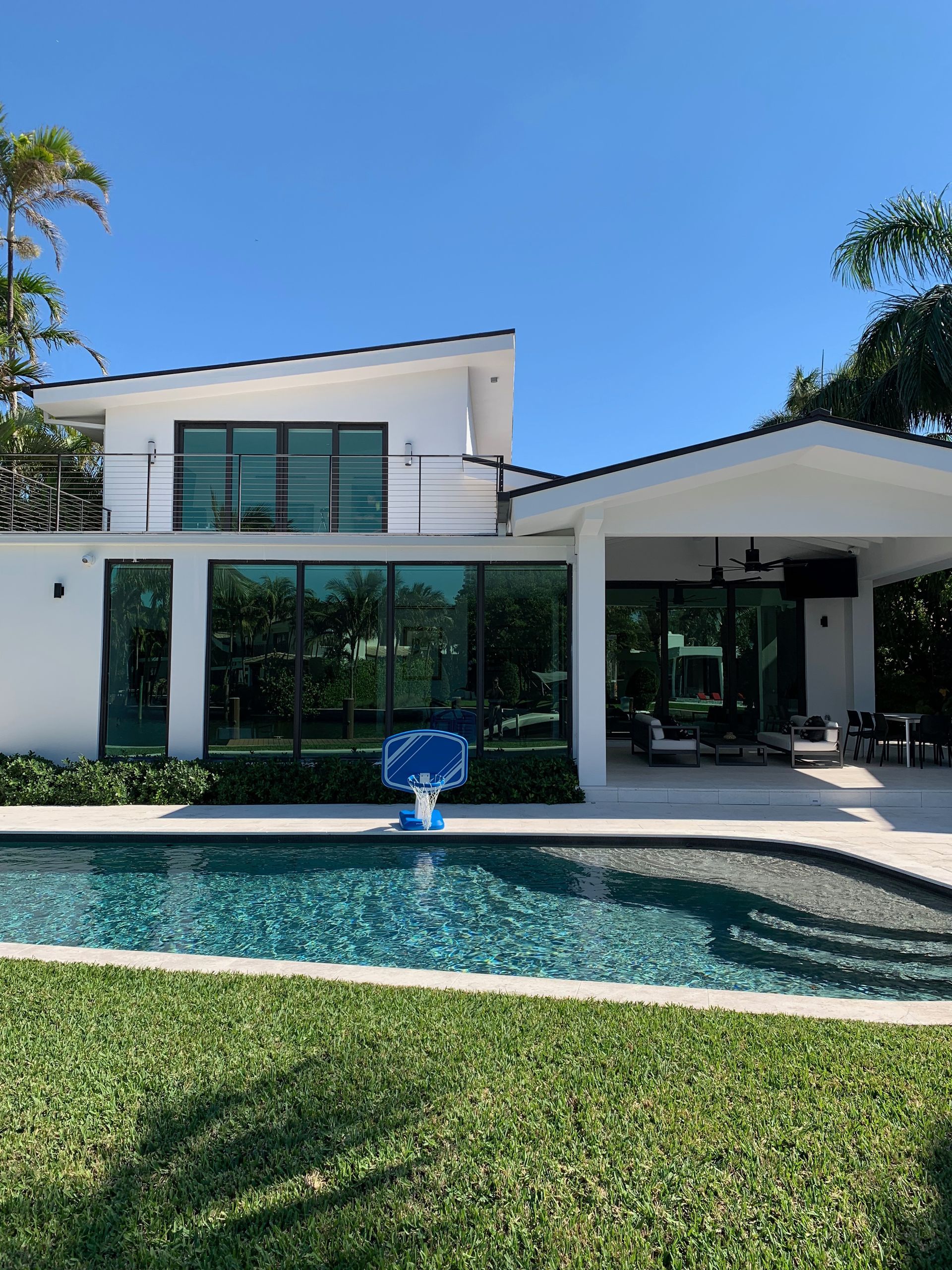 Modern white house with a pool, patio, and lush green lawn on a sunny day.