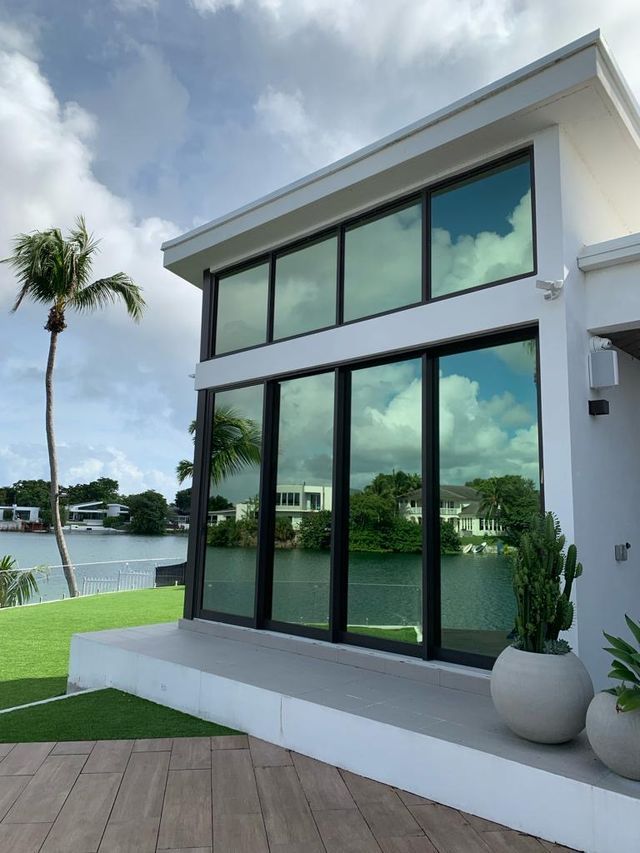 Modern white house with large tinted windows overlooking a waterway, blue sky.
