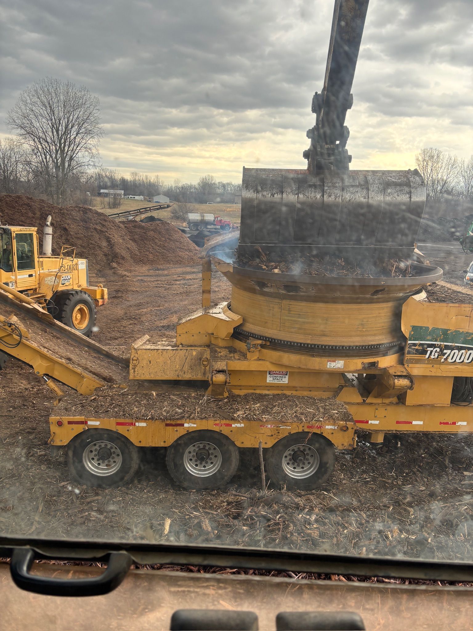 Yellow construction machinery with a large rotating attachment on a flatbed trailer in a muddy worksite