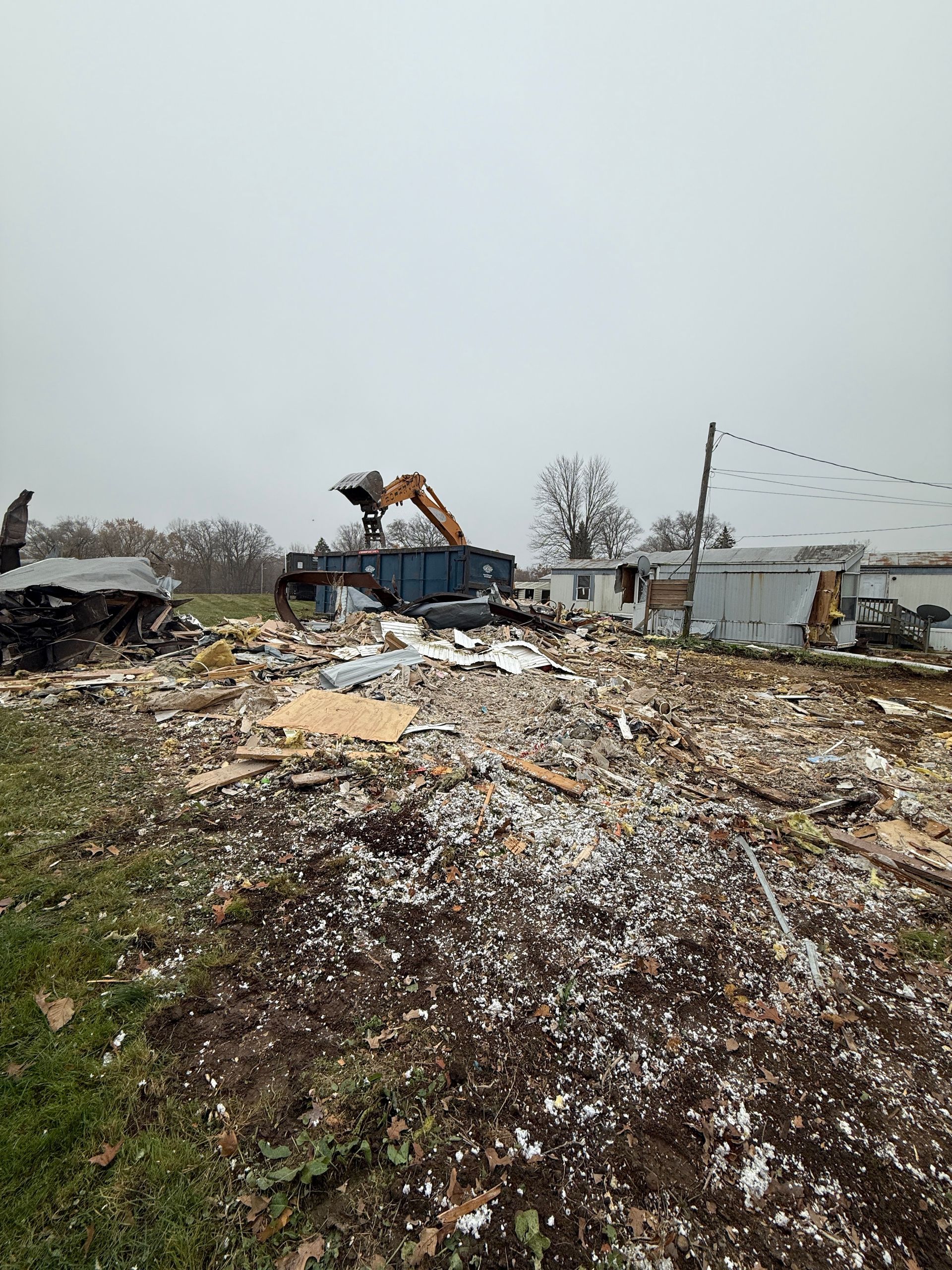 Bulldozer on a debris-strewn lot under an overcast sky, with damaged buildings in the background
