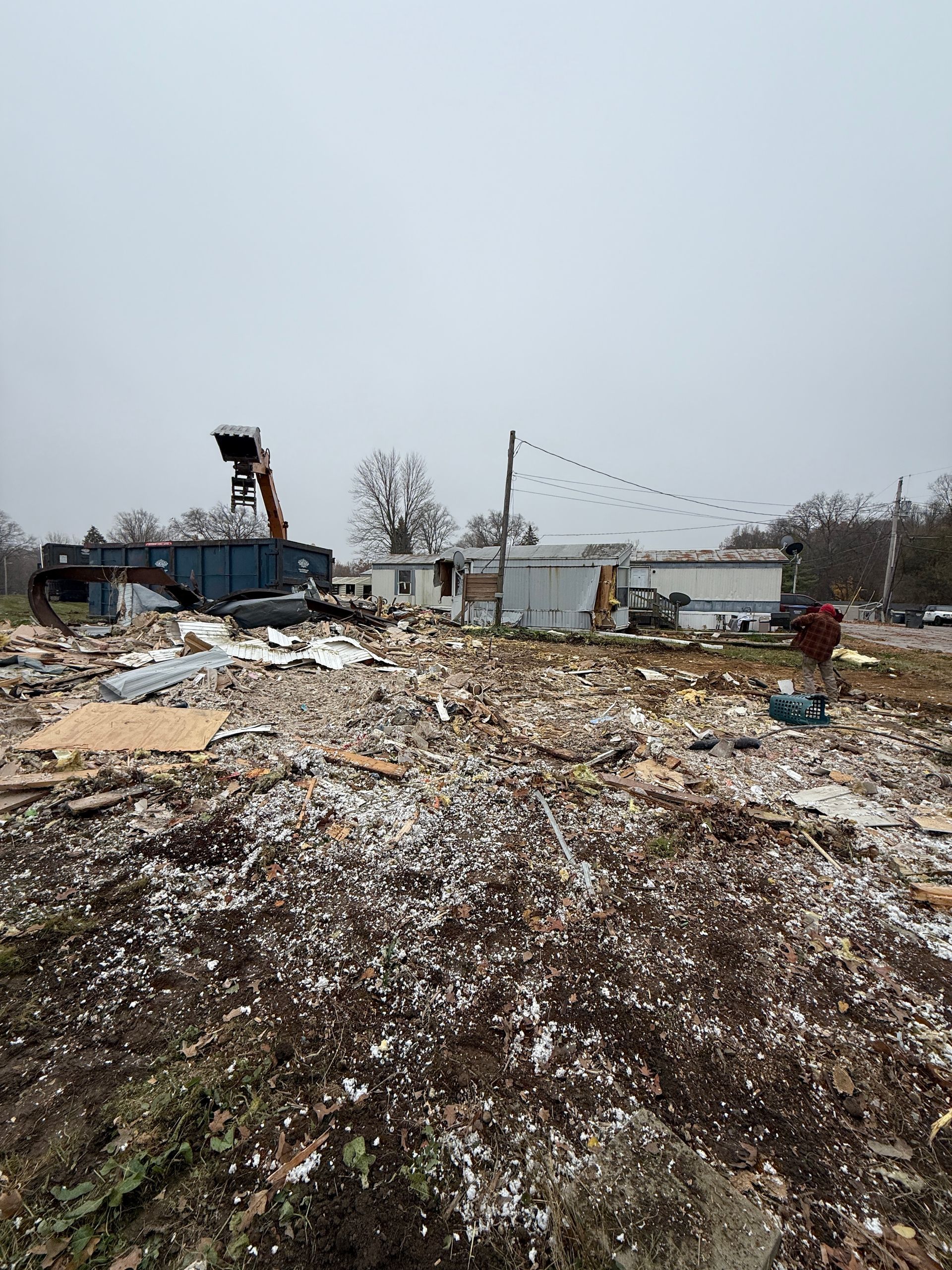 Snow-dusted rubble and debris in a damaged lot, with a crane and partially collapsed building in the background
