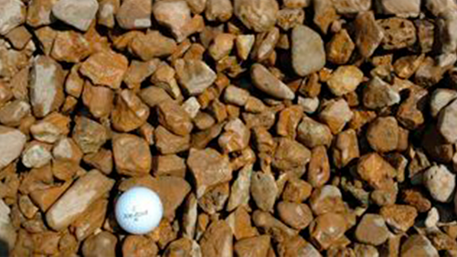 White golf ball resting among brown rocks in a gravel bed.