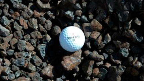 White golf ball resting on dark gravel rocks, with small printed text visible on top