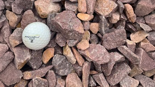 White golf ball on reddish gravel rocks.