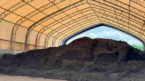 Large pile of dark soil under a beige arched storage shelter with daylight opening at the far end