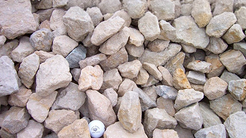 Pile of light-colored rocks and gravel, with a small white ball near the bottom