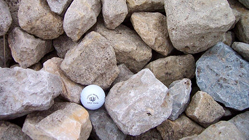 A golf ball nestled among tan and gray rocks.