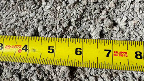 Yellow measuring tape stretched across gray gravel, showing inches 4 to 8.