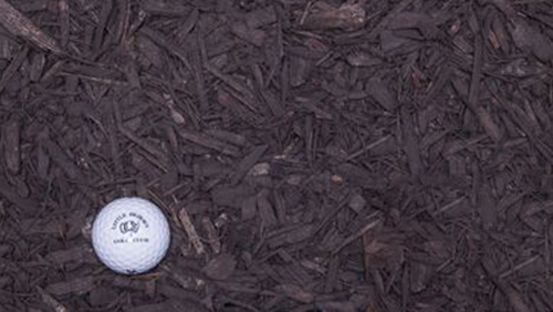 White golf ball on dark wood chips near the lower left corner