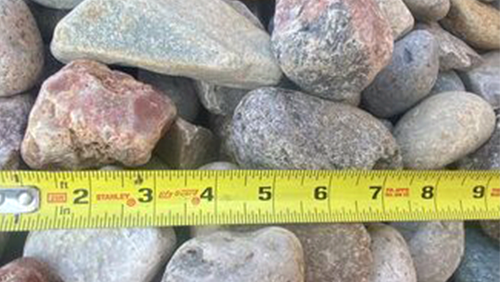 Rocks and pebbles beside a yellow measuring tape showing inches across the bottom