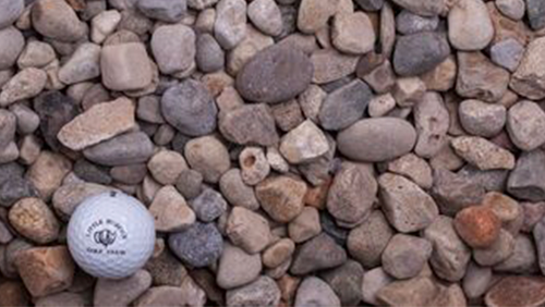 White golf ball on a bed of small brown and gray pebbles