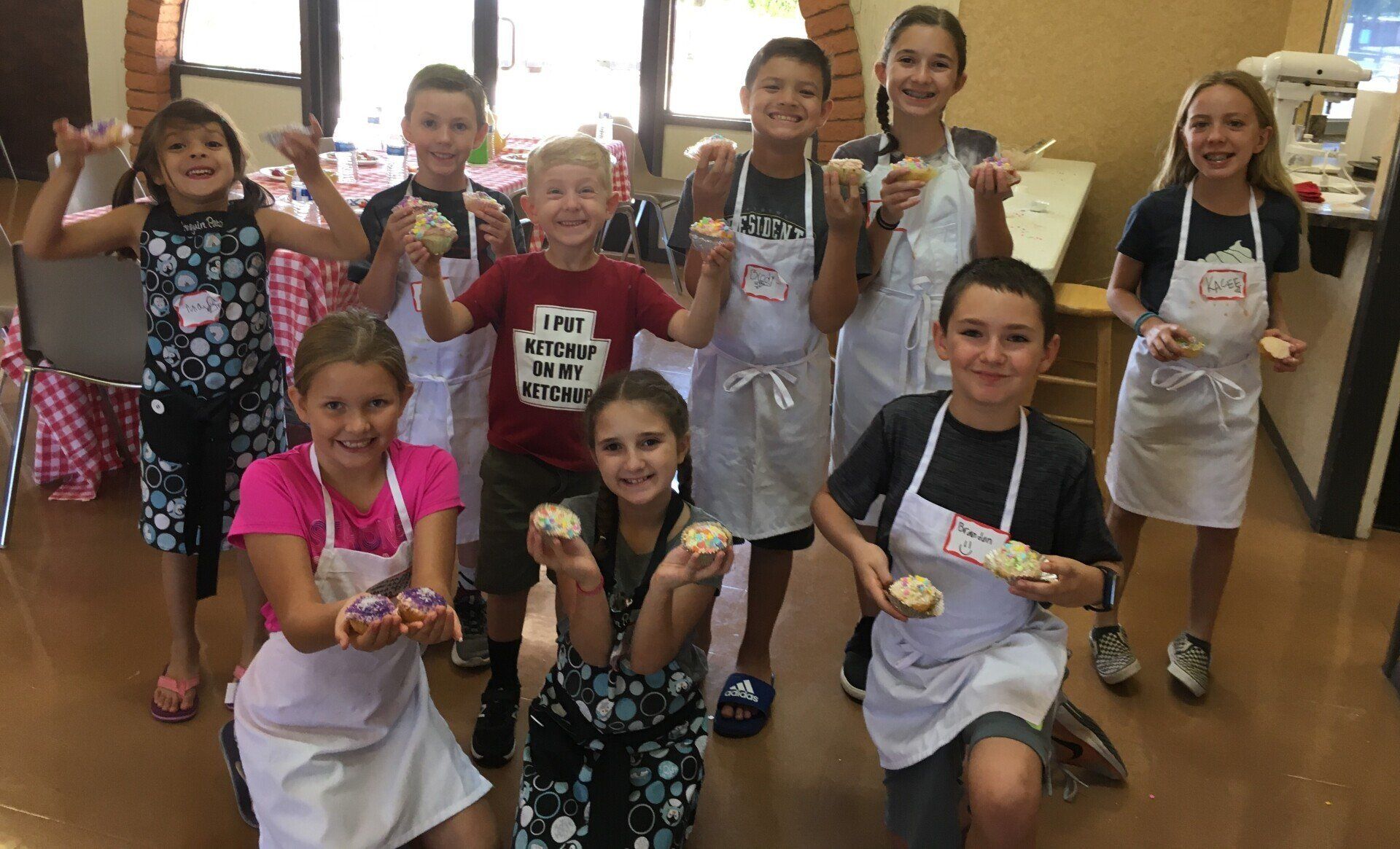 A group of children wearing aprons are holding cupcakes in their hands.