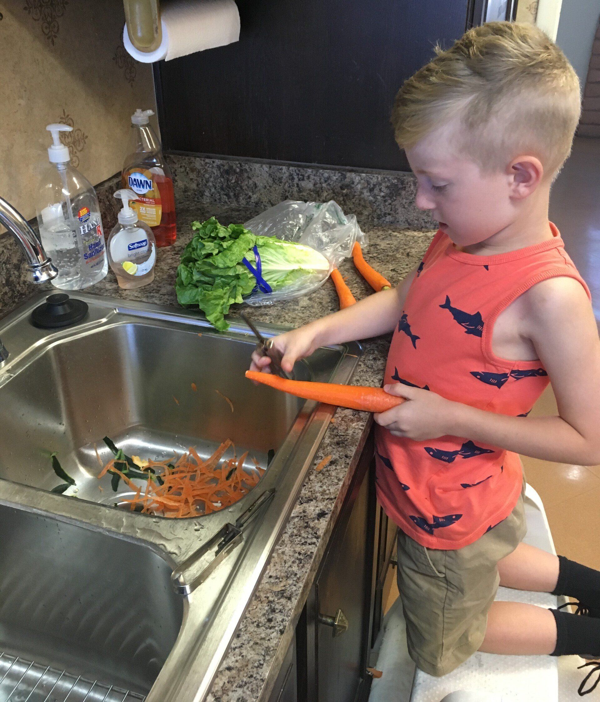 A young boy is washing carrots in a kitchen sink