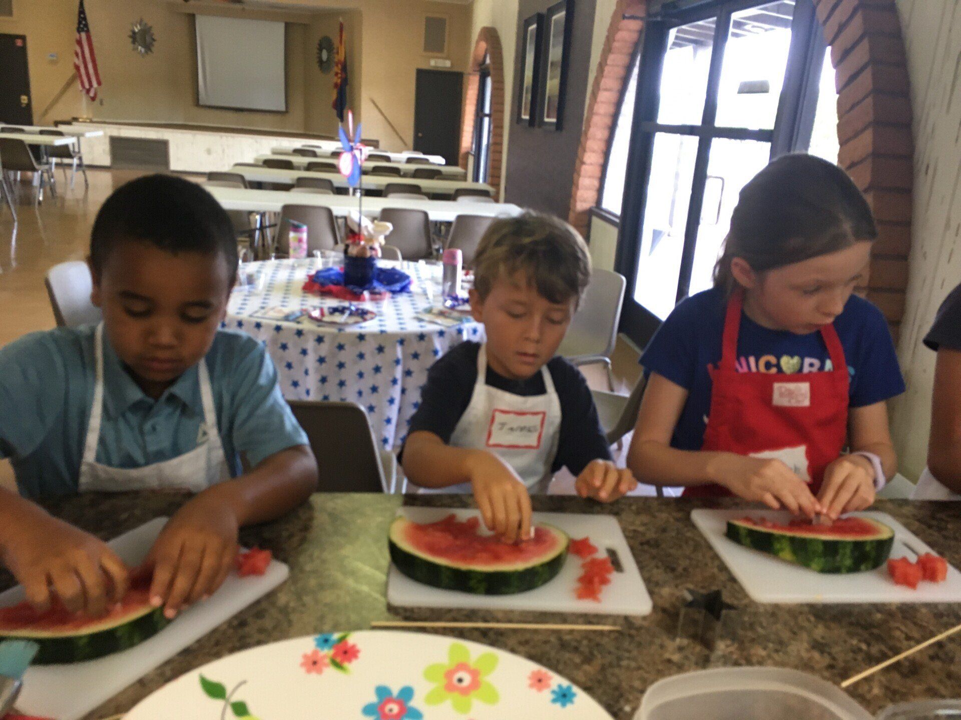A girl wearing an apron that says victoria is cutting a watermelon