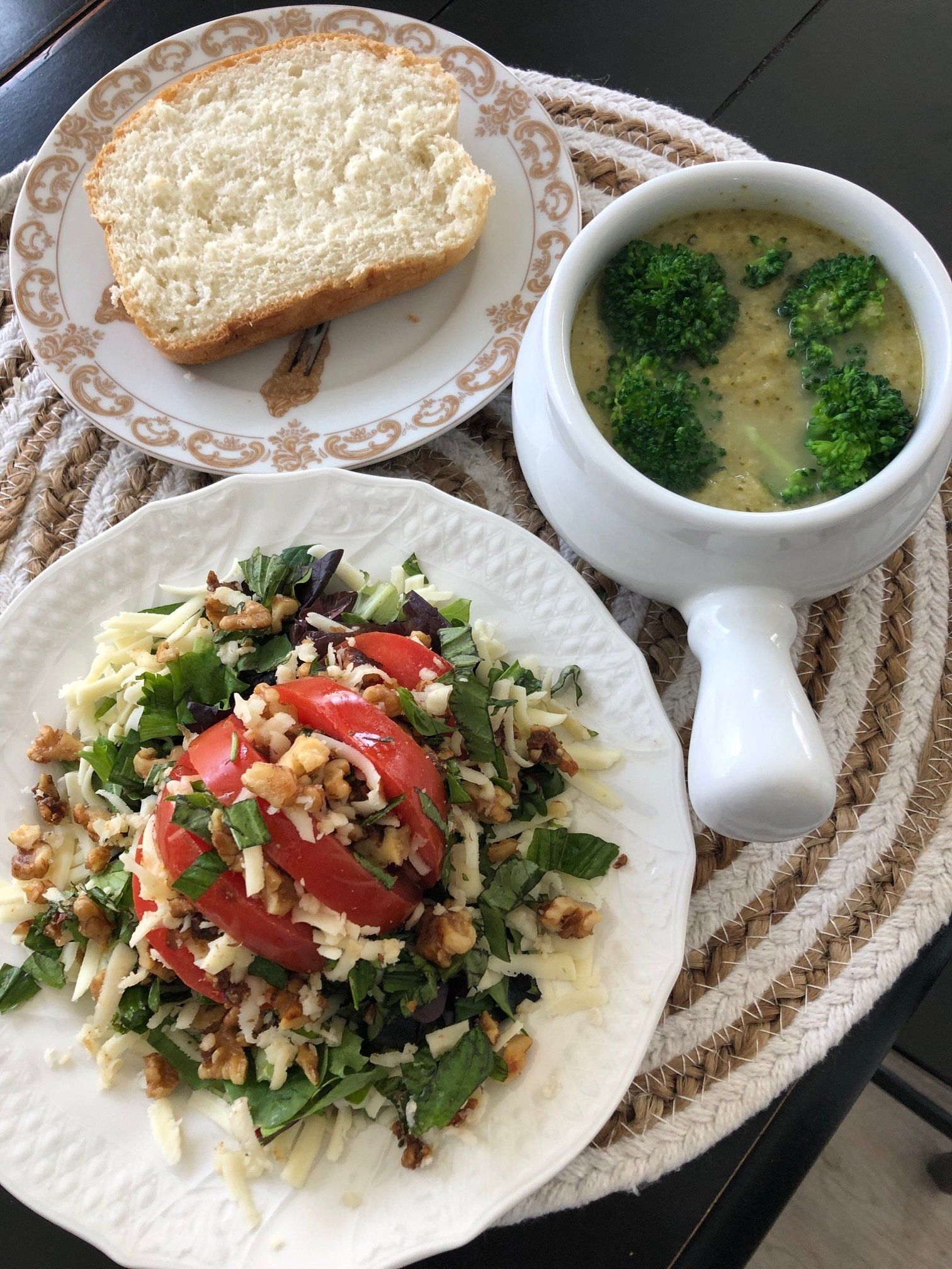 A plate of salad , a bowl of broccoli soup and a slice of bread on a table.