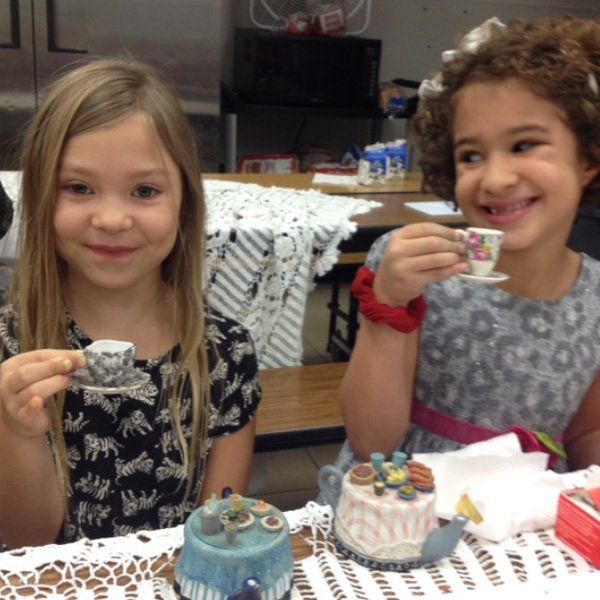 Two little girls are sitting at a table drinking tea