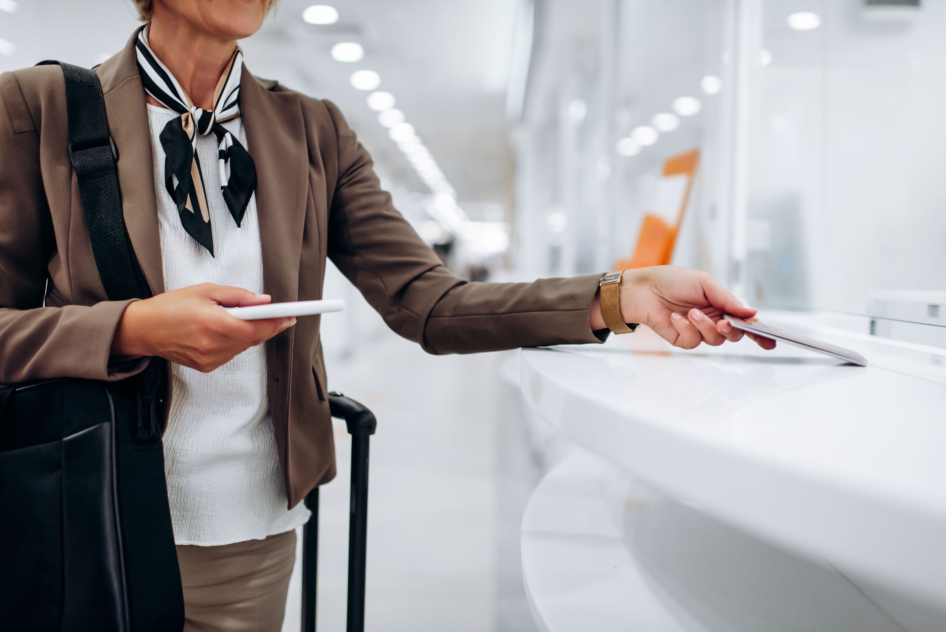 Donna in aeroporto che fa il check-in, con in mano telefono e passaporto, vicino ai bagagli.