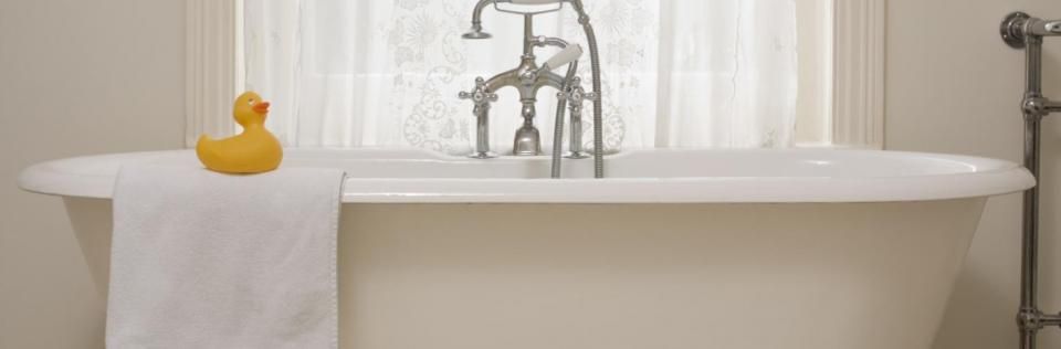 White bathtub with chrome faucet, white towel, and a yellow rubber duck in a bright bathroom
