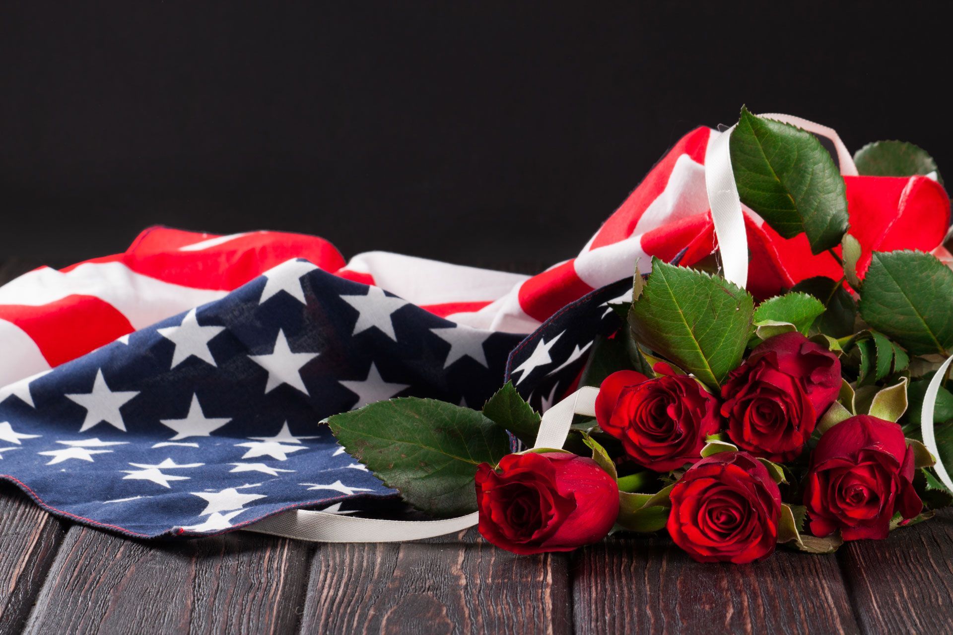 American flag draped over a wooden surface, alongside a bouquet of red roses.