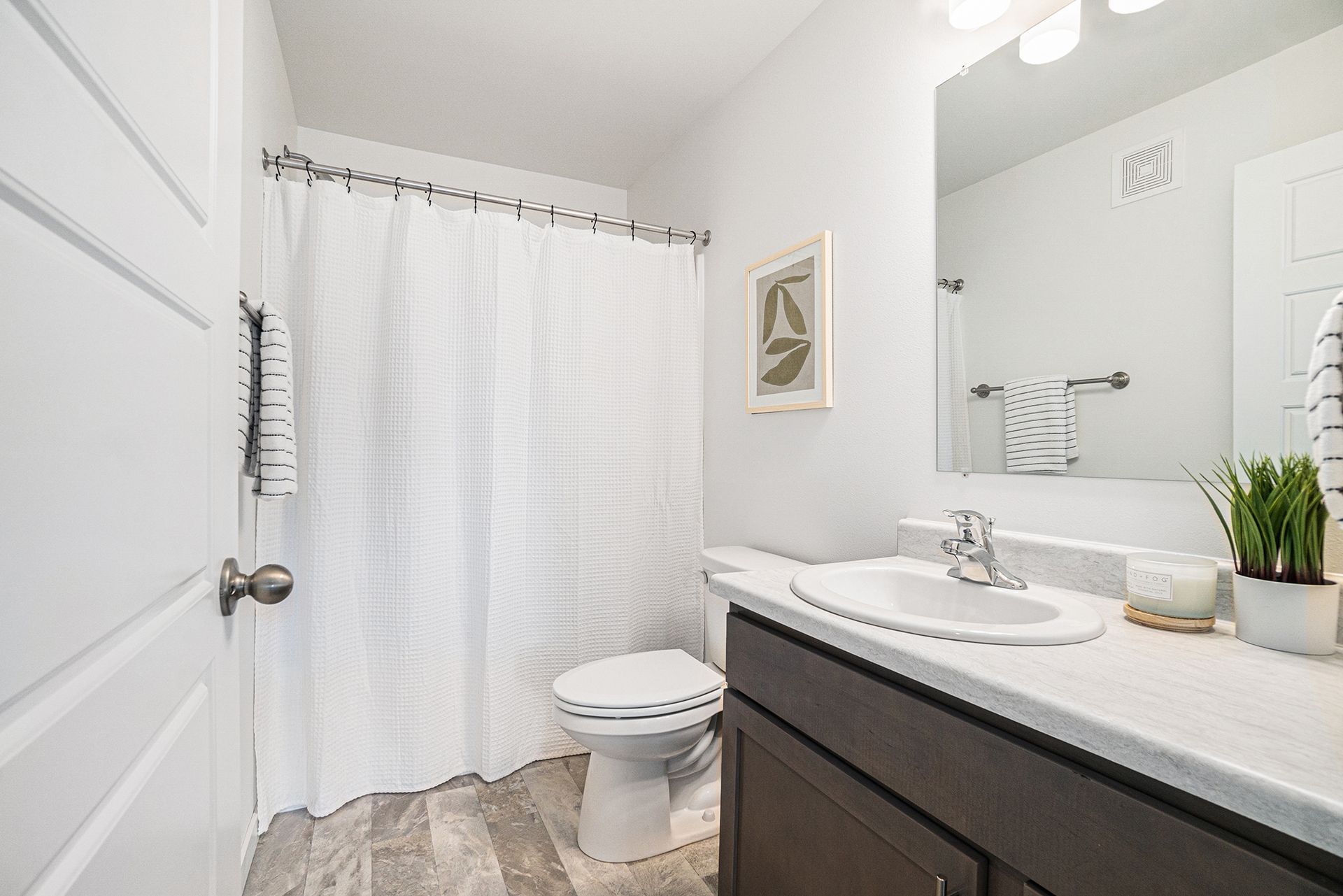 A bathroom with a toilet , sink , mirror and shower curtain.