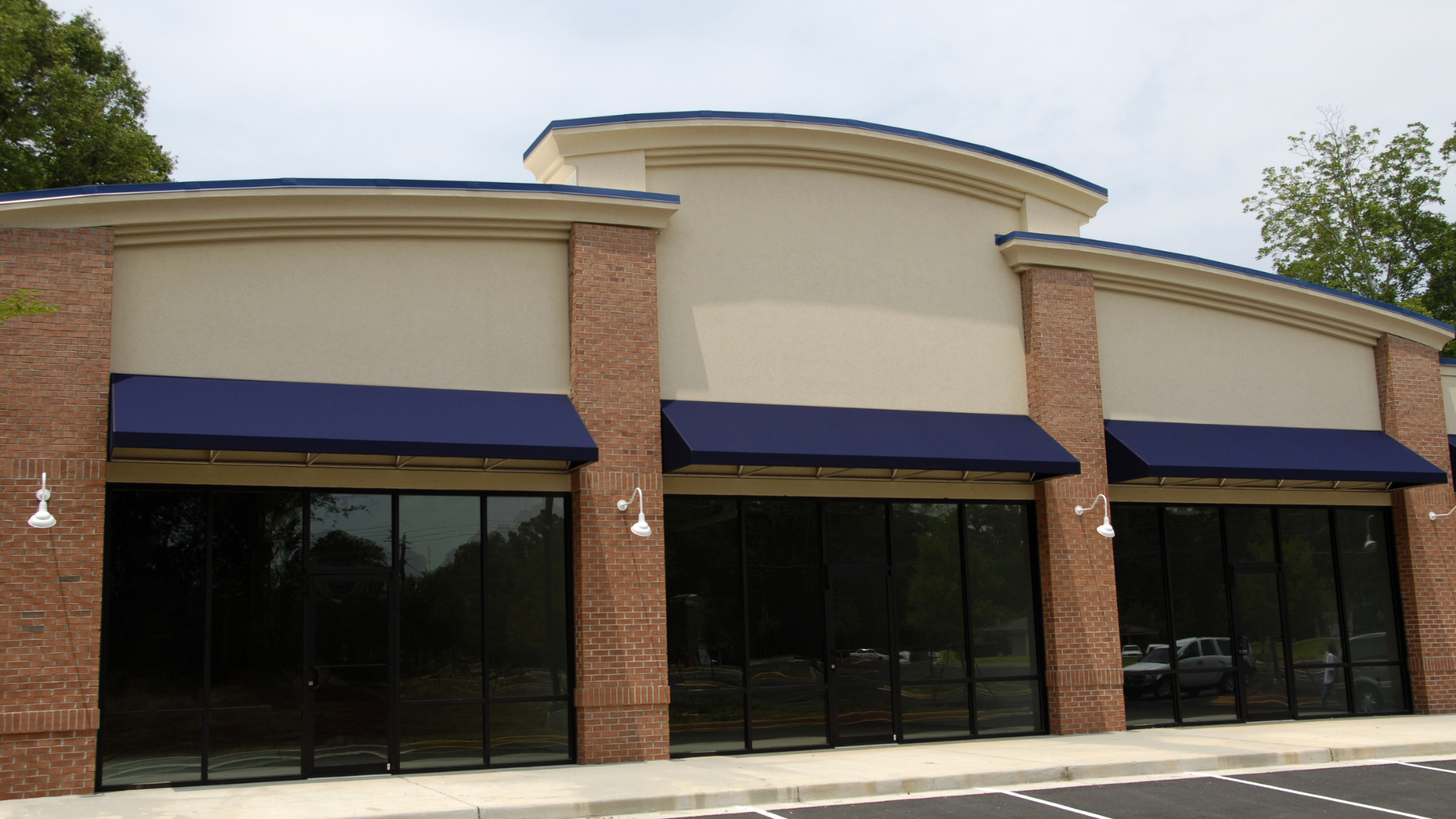 An empty store front with blue awnings and a parking lot in front of it.
